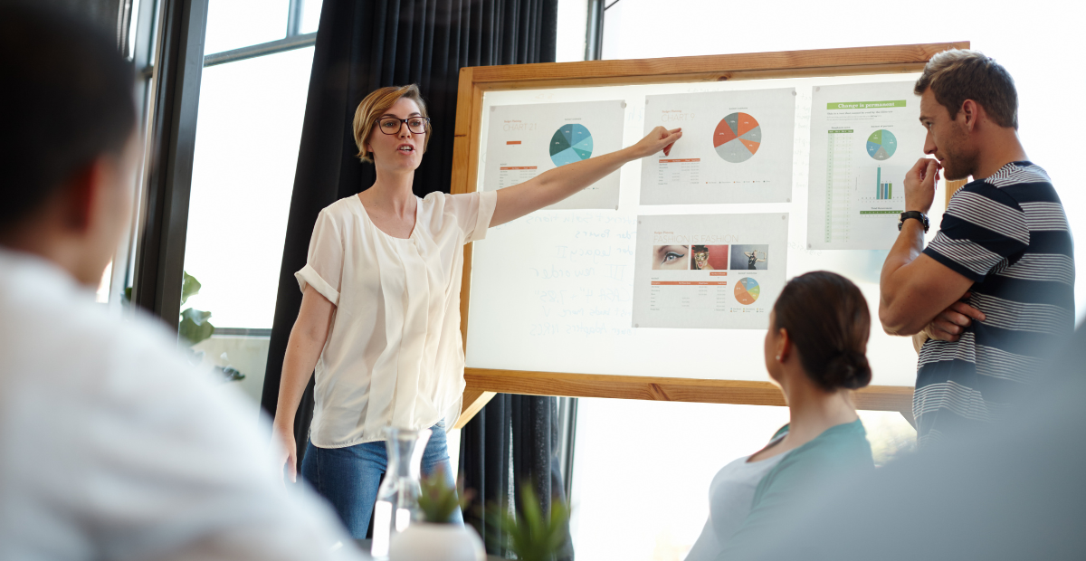 a woman pointing at charts on a board as people look on and nod.