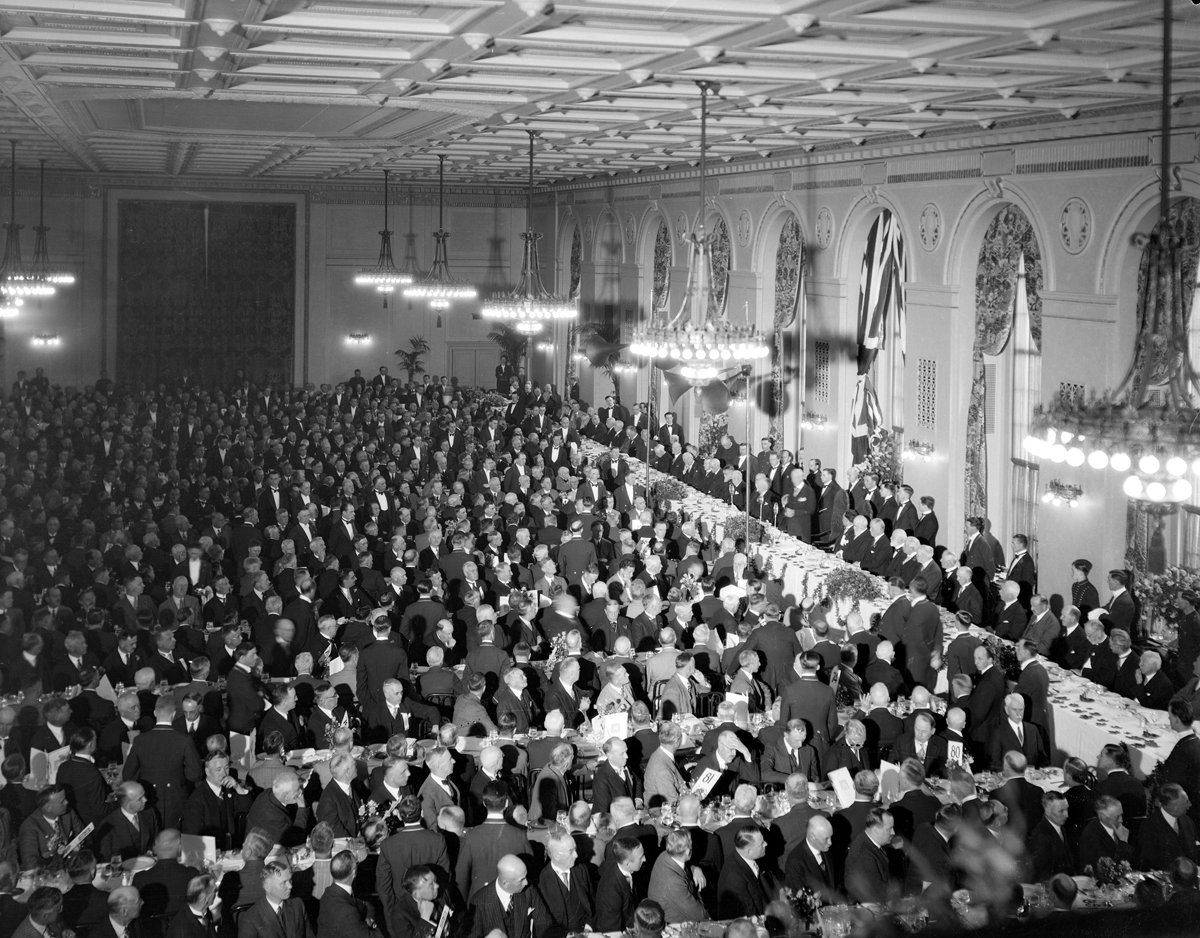 Black and white photo of a large hall full of men in suits