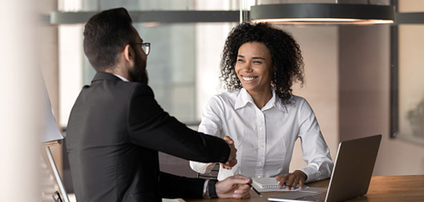 A Black woman and white man smiling and shaking hands